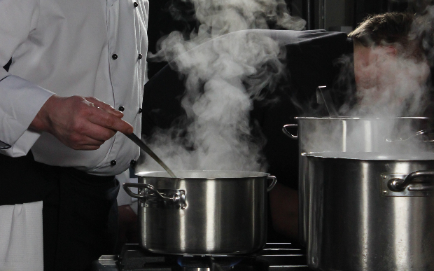Koch steht an dampfenden Kochtöpfen - Schimmel am Arbeitsplatz ist in Großküchen besonders kritisch