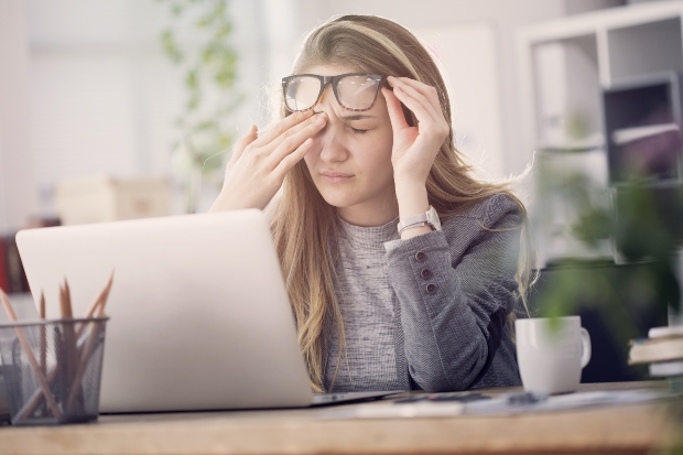 Junge Frau am Schreibtisch reibt sich die Augen - Aspekte für gesundes Wohnen