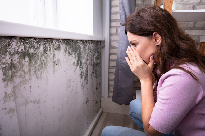 Frau hält sich die Hände vors Gesicht, Schimmel an der Wand