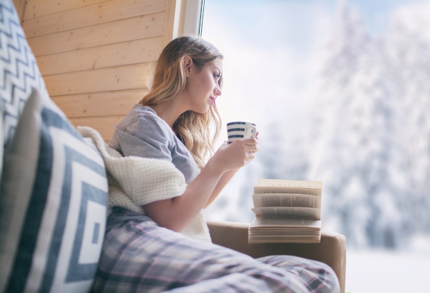 Junge Frau sitzt im Winter mit Becher Kaffee oder Tee am Fenster