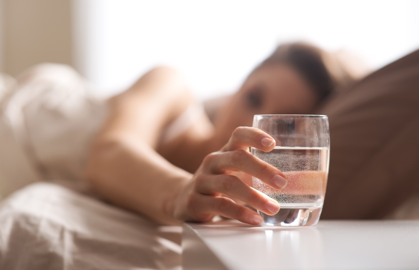 Frau im Bett greift nach Glas Wasser - Trockener Hals als Problem