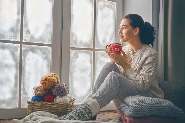 Frau sitz im Winter am Fenster und trinkt Tee