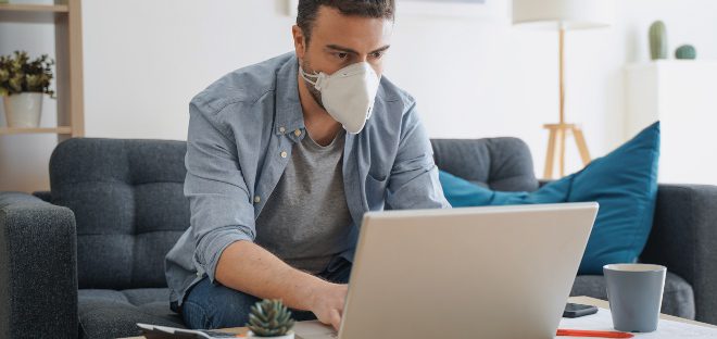 Mann mit Schutzmaske am Laptop - Virenkonzentration beachten