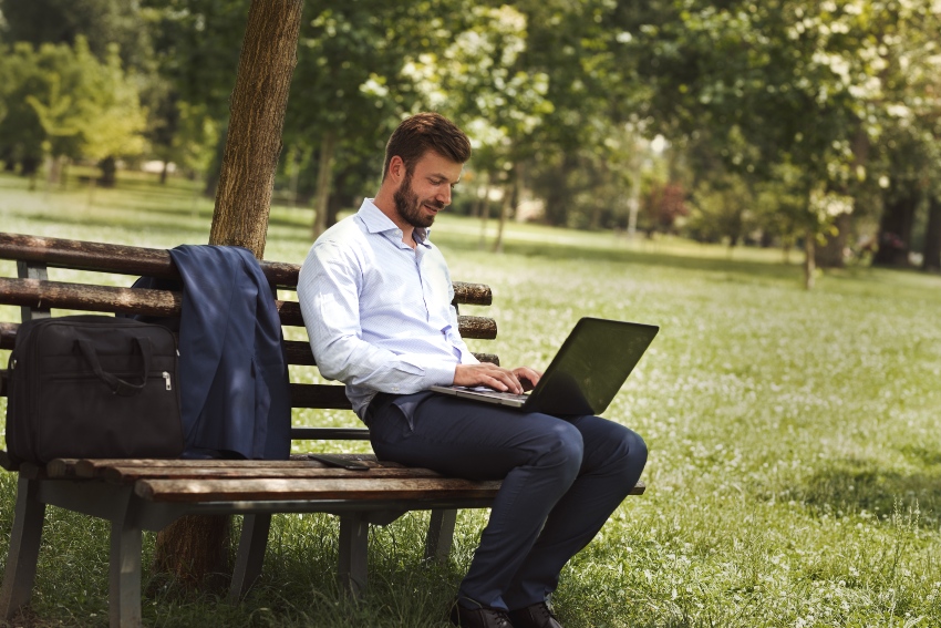 Junger Mann mit Laptop auf Park-Bank - mobiles Arbeiten ist nicht gleich Home-Office